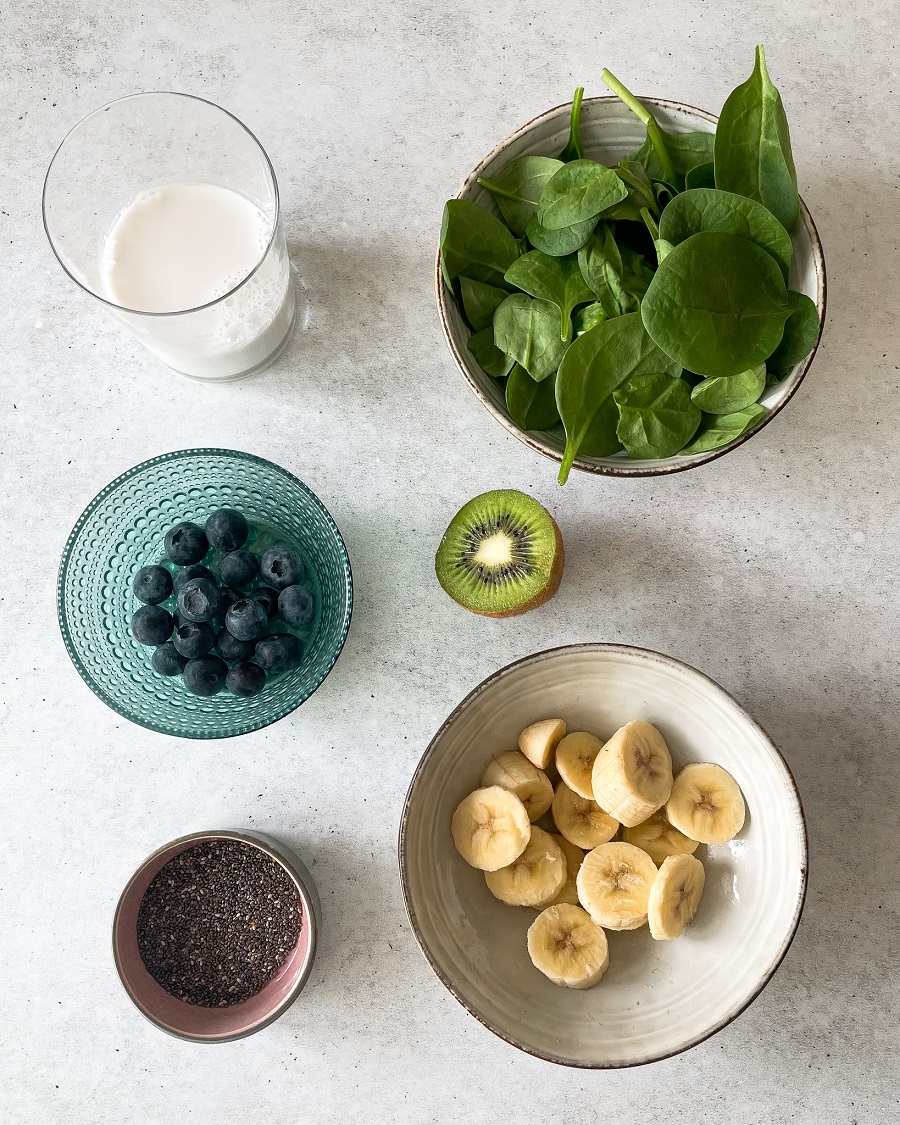 bowl of ingredients, milk, bluberries, kiwi, banana, chia seeds and spinach 